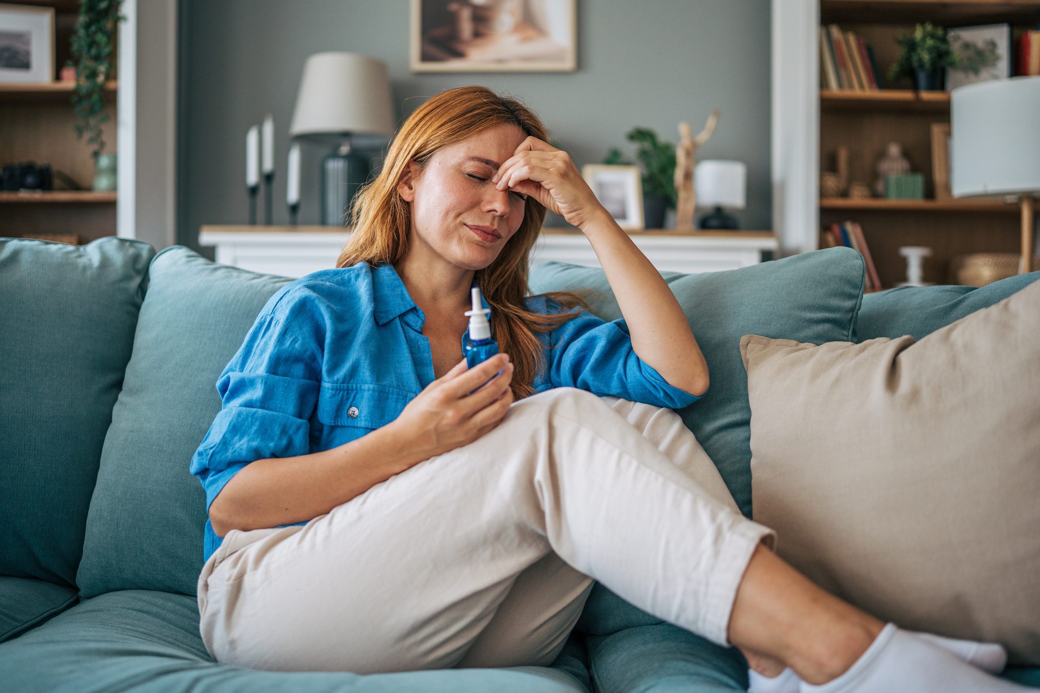 Woman holding nasal spray, rubbing forehead