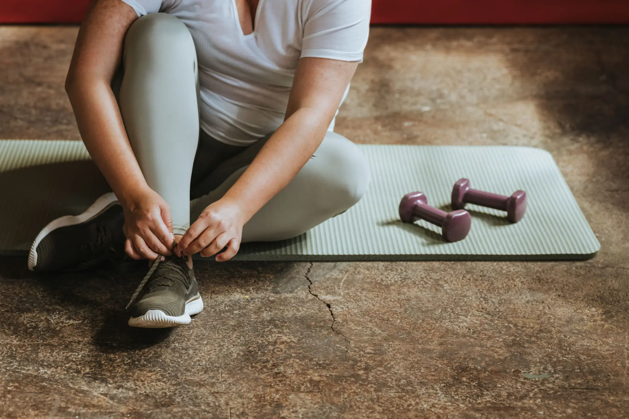 Person tying shoe on yoga mat near dumbbells