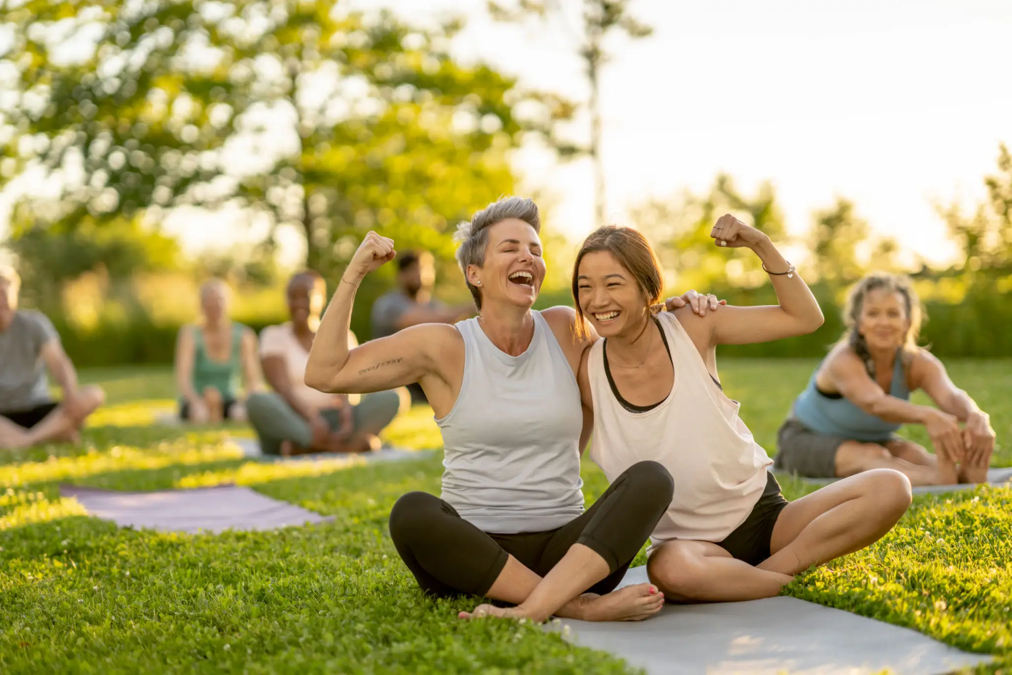 Two women flexing arms at outdoor yoga class