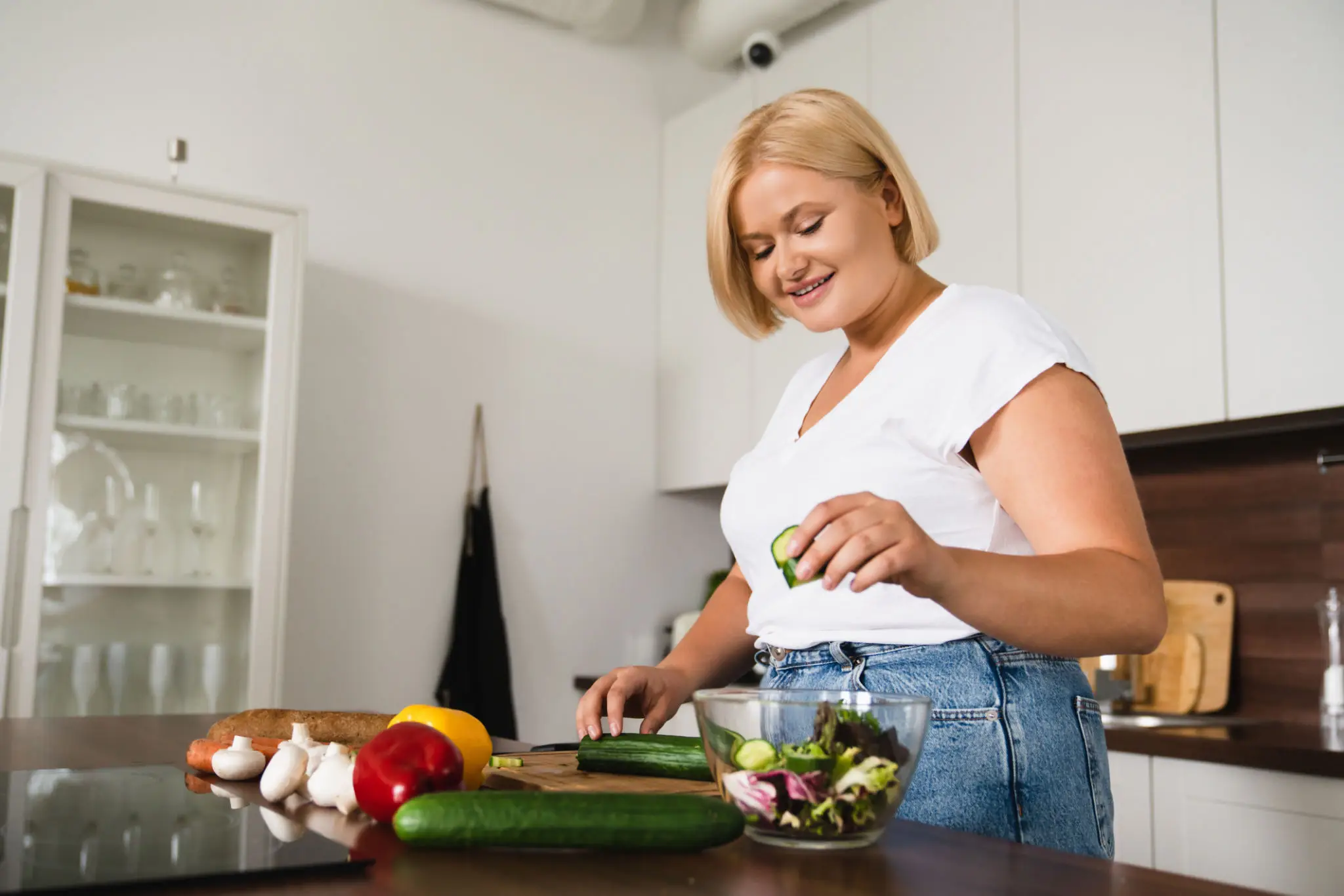 Smiling woman preparing salad with cucumber